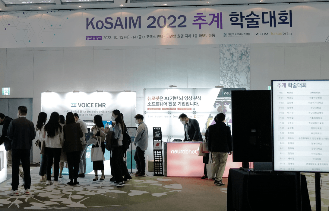 A busy exhibition booth at the KoSAIM 2022 conference showcasing the VoiceEMR solution. Attendees engage with staff, demonstrating interest in the medical AI technology.